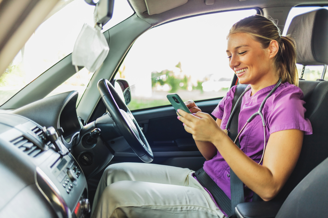 Nurse arriving at a patient's home, she is sitting in her car using her mobile phone. A nurse dressed in her scrubs uniform sitting in her stationary car, holding her mobile phone.